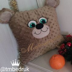 a teddy bear pillow sitting on top of a table next to an orange and christmas tree