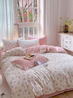 a bed with pink comforters and pillows in a bedroom next to a large window