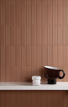 a coffee cup sitting on top of a white shelf next to a brown tile wall