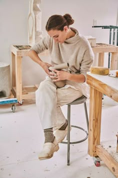 a woman sitting on top of a stool holding a cell phone next to a wooden table