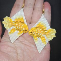 a pair of yellow and white fish earrings in the palm of someone's hand