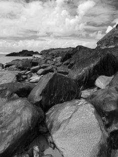 black and white photograph of rocks on the beach with clouds in the sky behind them