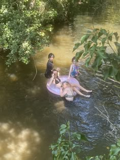 four people are floating on an inflatable raft down a river with trees around them