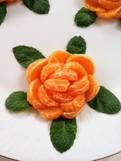 there is an orange flower made out of leaves on a white plate with green leaves