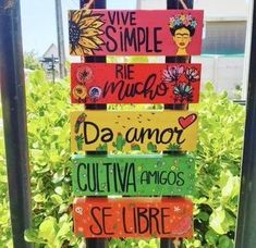 a wooden sign with spanish words hanging from it's side in front of some bushes