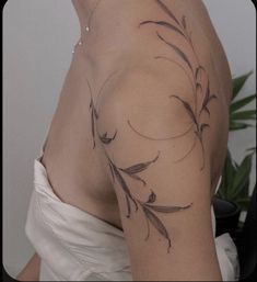 the back of a woman's shoulder with flowers and leaves tattooed on her arm