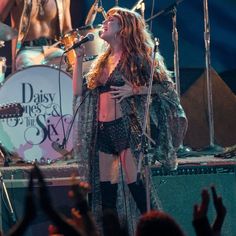 a woman singing into a microphone while standing in front of an audience at a concert