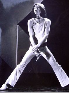 a woman in white pants standing on one leg with her hands behind her back and legs crossed