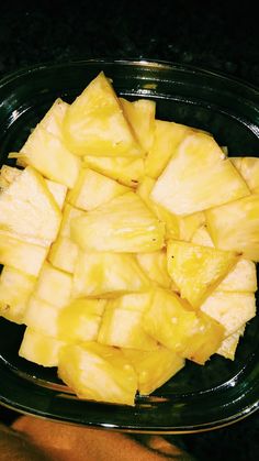 sliced pineapple in a glass bowl on a black counter top with someone's hand next to it