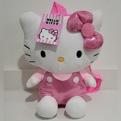 a hello kitty stuffed animal with a pink bow on its head, sitting in front of a white wall