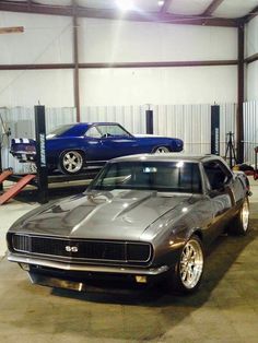 two muscle cars parked in a garage next to each other and one is shiny silver