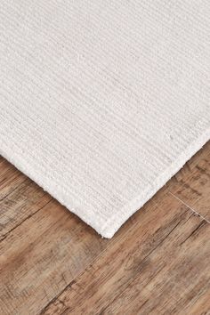 a white rug on top of a wooden floor with a wood flooring board in the background