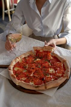 a woman sitting at a table with a pizza and glass of wine