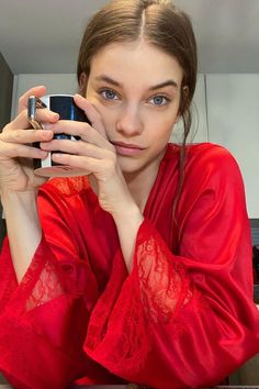 a woman taking a selfie with her cell phone in front of her face and wearing a red robe