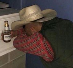 a man wearing a cowboy hat leaning against a counter with a beer in his hand