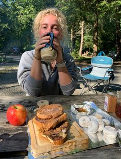 a woman sitting at a picnic table drinking from a cup