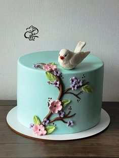 a blue cake decorated with flowers and a bird on the top is sitting on a plate