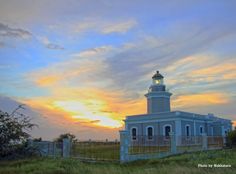 a light house sitting on top of a lush green field next to a fenced in area