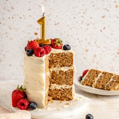 a slice of cake with white frosting and strawberries on the side, next to a piece of one - year birthday cake