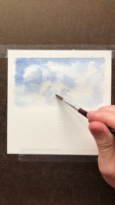 a person holding a paintbrush in front of a piece of paper with watercolor on it