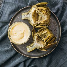 some artichokes on a plate with a bowl of mustard and sauce next to it