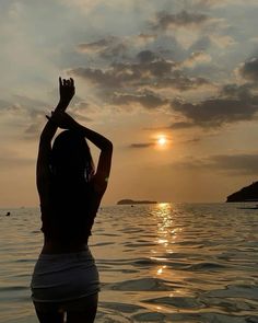 a woman standing in the water with her arms raised up to the sun behind her