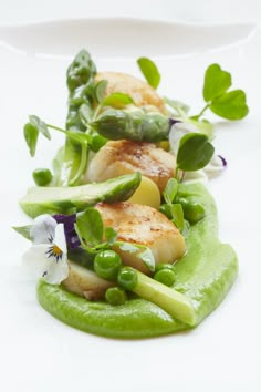 a white plate topped with green vegetables and scallops