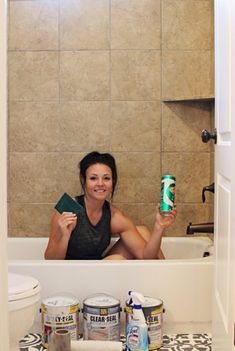 a woman sitting in a bathtub holding a can of paint