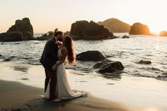 a bride and groom kissing on the beach at sunset