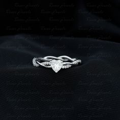 a white gold ring with a heart shaped diamond on it's side, sitting on top of a black cloth