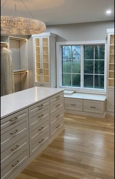 an empty kitchen with white cabinets and wood flooring in front of a large window