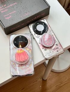 two cell phones sitting on top of a table next to a box with a candle in it