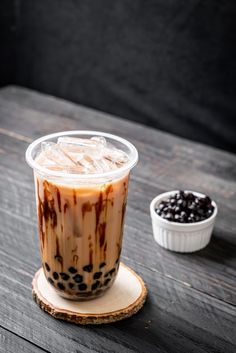 an iced drink with chocolate chips on the side sitting on a wooden table next to a small bowl of blackberries