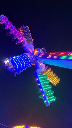 an amusement park ride lit up at night with colorful lights on it's sides