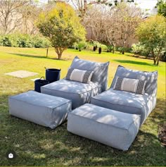 two gray couches with matching cushions in the grass near trees and bushes, one is empty