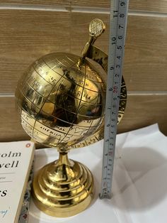 a small golden globe sitting on top of a table next to a ruler and book