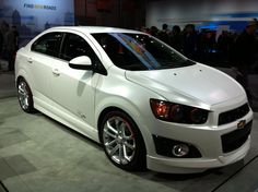 a white chevrolet car is on display at an auto show with people looking in the background