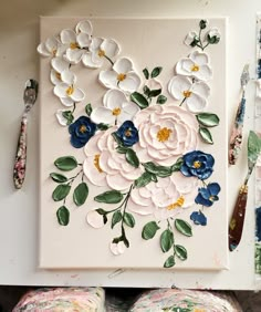 a painting with flowers on it next to some paintbrushes and other art supplies