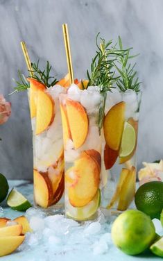 two glasses filled with fruit and ice next to limes, lemon wedges and flowers