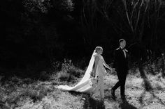 a bride and groom walking through the woods together in black and white photo with long veil