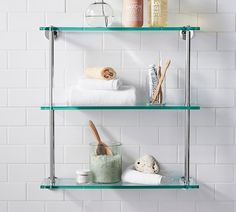 two glass shelves with towels, soap and other items on them against a white tiled wall