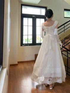 a woman in a white dress is looking out the window at some stairs and windows