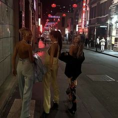 three women are walking down the street at night in high heels and wide leg pants