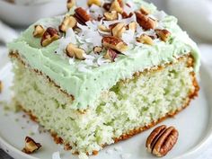 a piece of cake with green frosting and pecans on top, sitting on a white plate