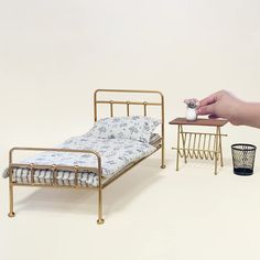 a miniature bed and side table with a person reaching for the pillow on one end