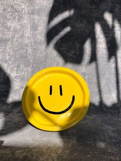 a yellow plate with a smiley face drawn on the surface next to a shadow of a palm tree