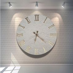 a large clock mounted to the side of a white brick wall in an empty room