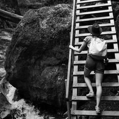 a person with a backpack climbing up a wooden ladder over a stream in the woods