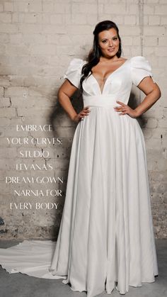 a woman standing in front of a brick wall wearing a white dress with ruffle sleeves