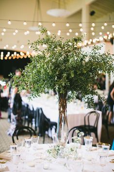 the table is set for an event with white linens and greenery in a vase